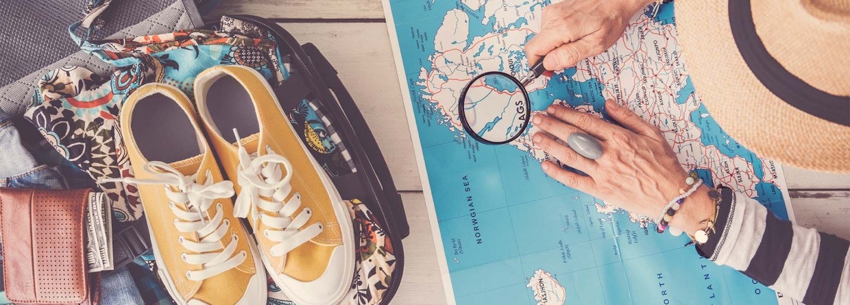 Voorpret vakantie; vrouw bekijkt een landkaart met een loep ernaast stat een ingepakte koffer