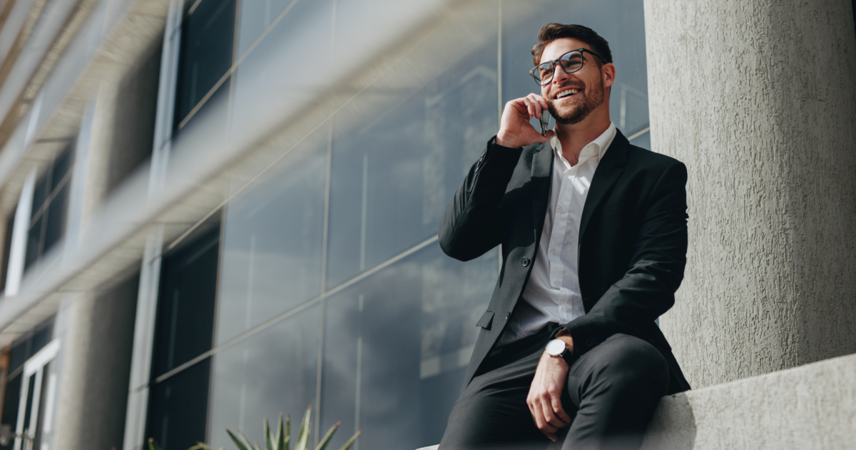 Lachende zakenman die buiten zit en een mobiele telefoon gebruikt