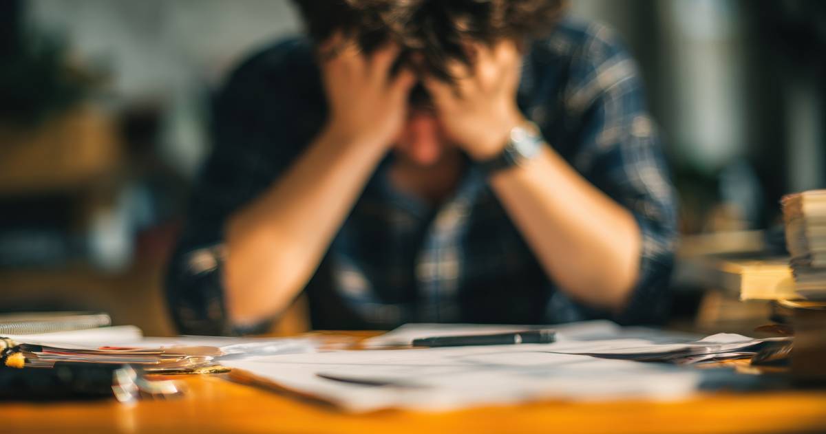 stress; man zit met handen op zijn voorhoogd achter zijn bureau