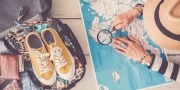 Voorpret vakantie; vrouw bekijkt een landkaart met een loep ernaast stat een ingepakte koffer