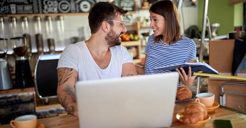 Jong stel praat en lacht terwijl ze ontbijten in het koffiehuis dat ze op het punt staan ​​te openen.