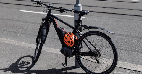 Elektrische fiets met een oranje helm staat tegen een lantaarnpaal aan