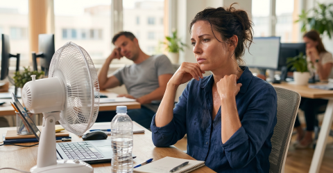 Extreme hitte op de werkvloer; vrouw op kantoor achter een ventilator